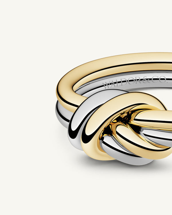 A polished stainless steel ring in 14k gold from Waldor & Co. One size. The model is Dual Knot Ring.