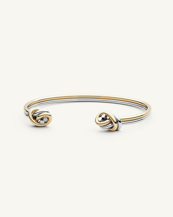 A polished stainless steel bangle in 14k gold from Waldor & Co. One size. The model is Dual Knot Twin Bangle.