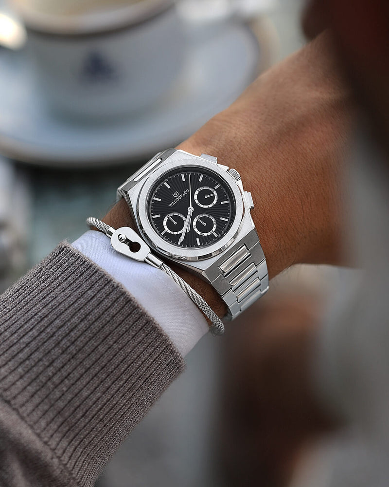 En rund herrklocka i rodiumpläterat silver från WALDOR & CO. med svart sunray urtavla och självlysande visare. Seiko urverk. Modellen är Inceptive 40 Azores.
